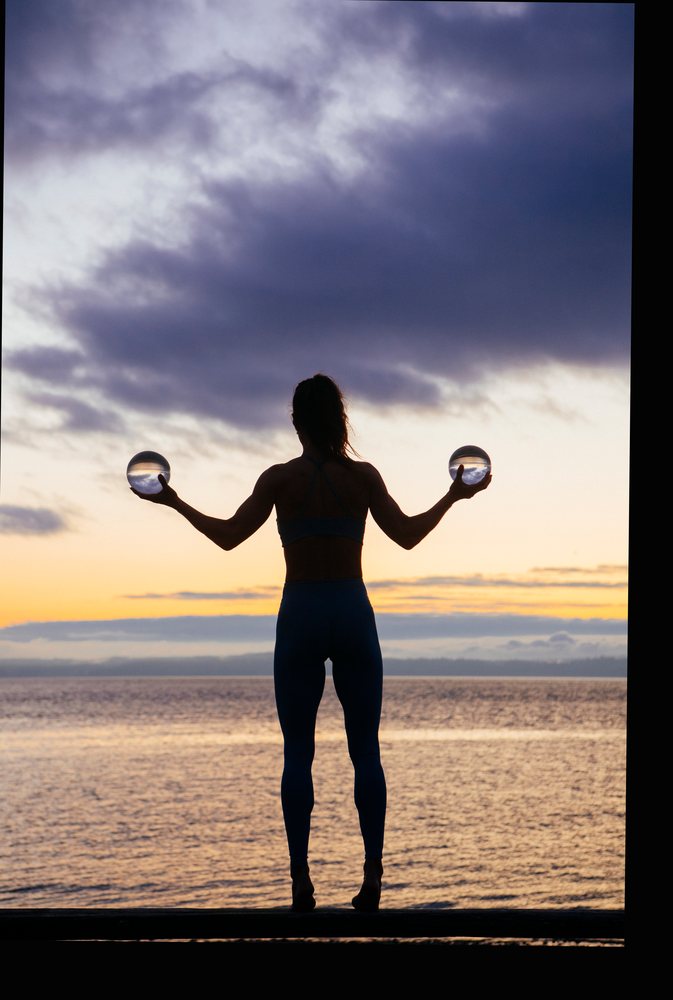 Silhouette of a woman holding two crystal balls standing at the waterfront during sunset, WA, USA.