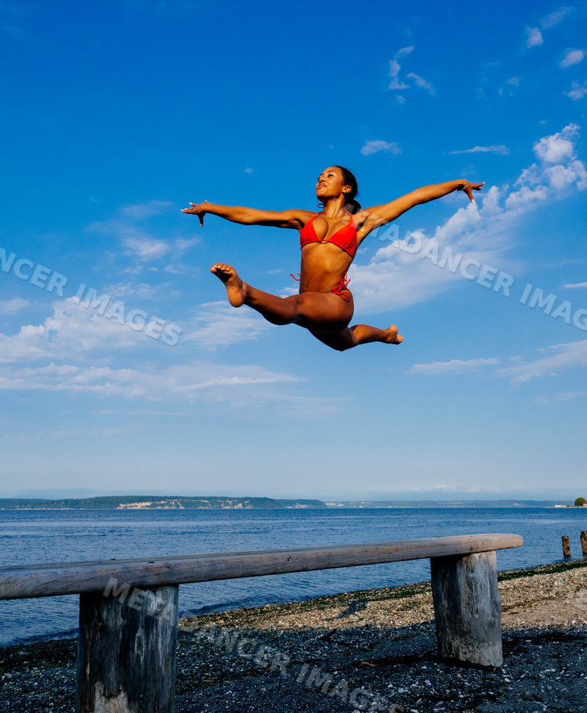 Woman in red swimwear performing a high leap on a beach balance beam