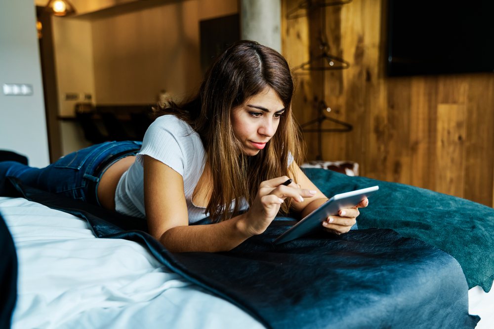 A woman using a tablet on a bed in a hotel room