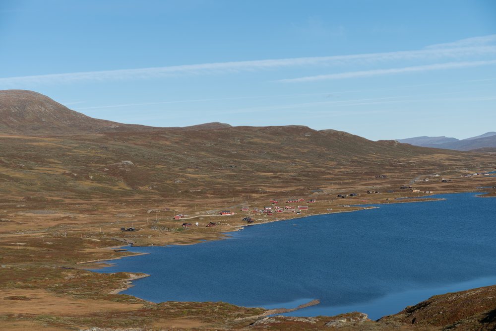 Scenic autumn view of a blue lake with red rural houses on hilly, rocky terrain, Norway.
