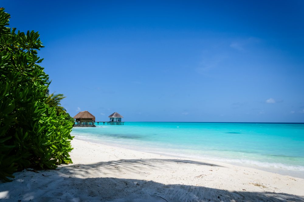 Tropical white sand beach with turquoise ocean and overwater huts under a clear blue sky, summer, Holliday, travel, landscape, Maldives.