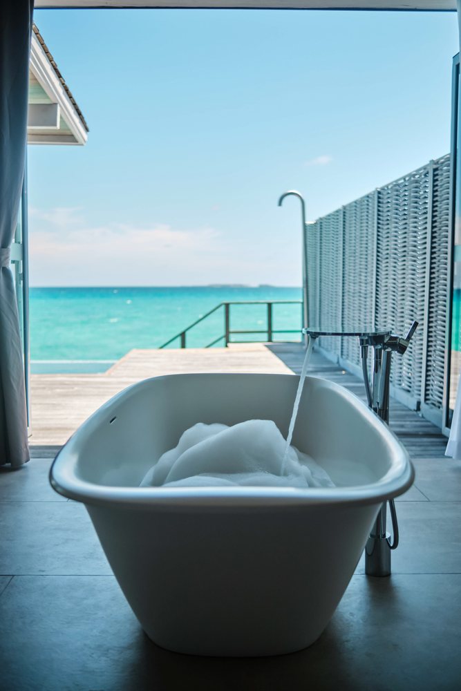 A modern freestanding bathtub with running water and bubbles overlooks a serene ocean view in the, Maldives.