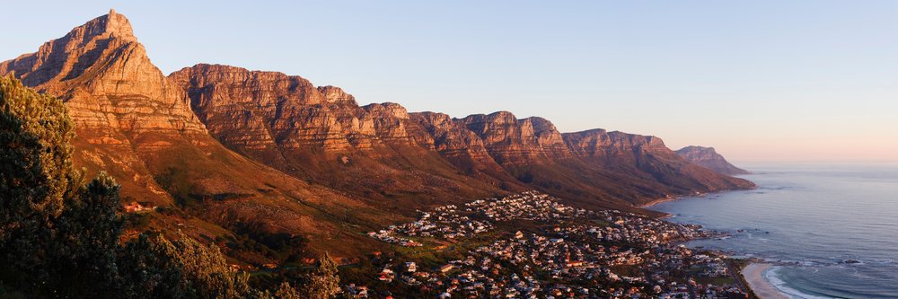 The Twelve Apostles mountain range overlooks the Camps Bay coastline at sunset, Western Cape, South Africa.