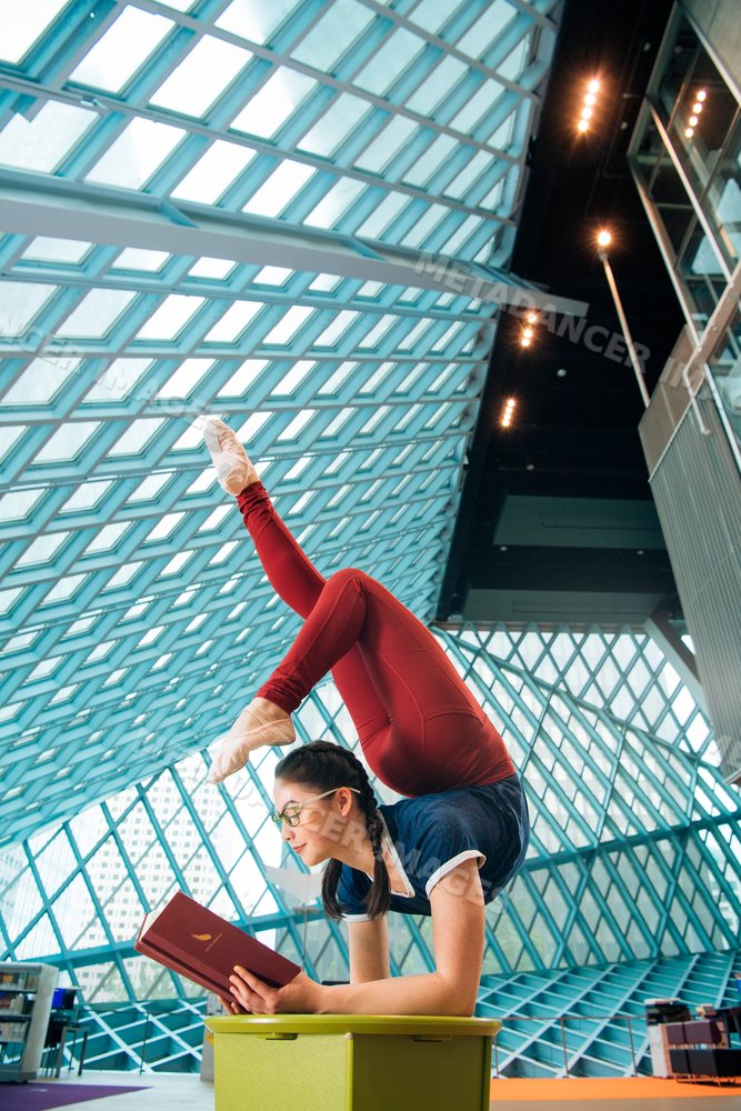 A woman reads a book while practicing a contortion pose in a library
