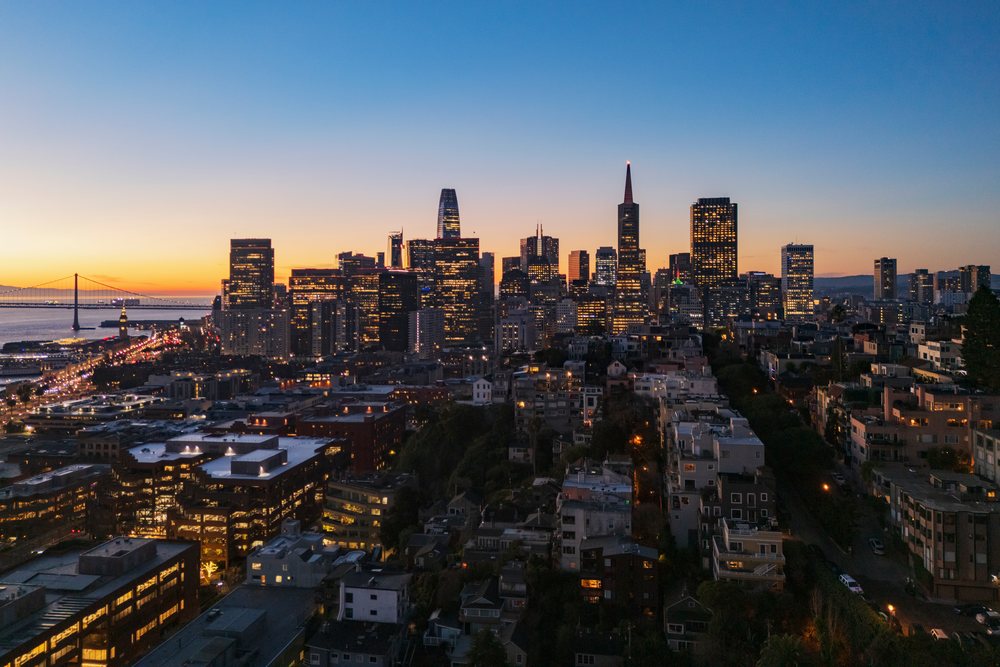 San Francisco downtown cityscape at Sunrise with buildings illuminated and the Bay Bridge visible over water, landscape, city life, California, USA.