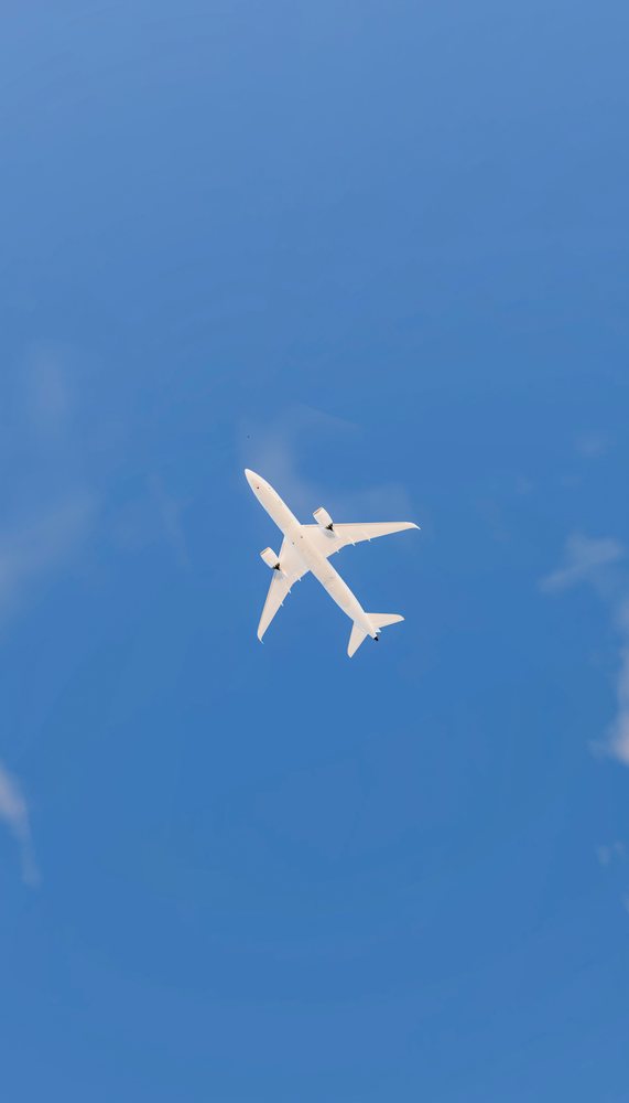 A white commercial airplane flying overhead against a clear blue sky, travel, fly, vacation.