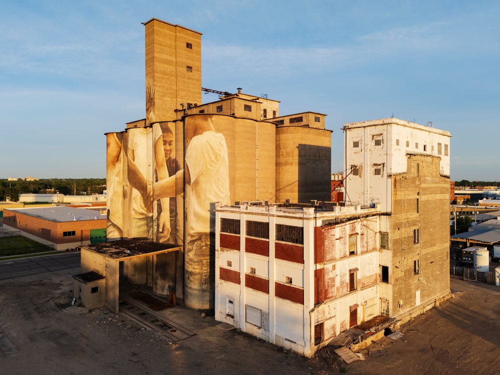 Grain Silo with a large mural of people painted on the exterior of an industrial building, USA under a clear sky, Weather, Environmental Issues, Storm Chasing, Salina, Kansas.