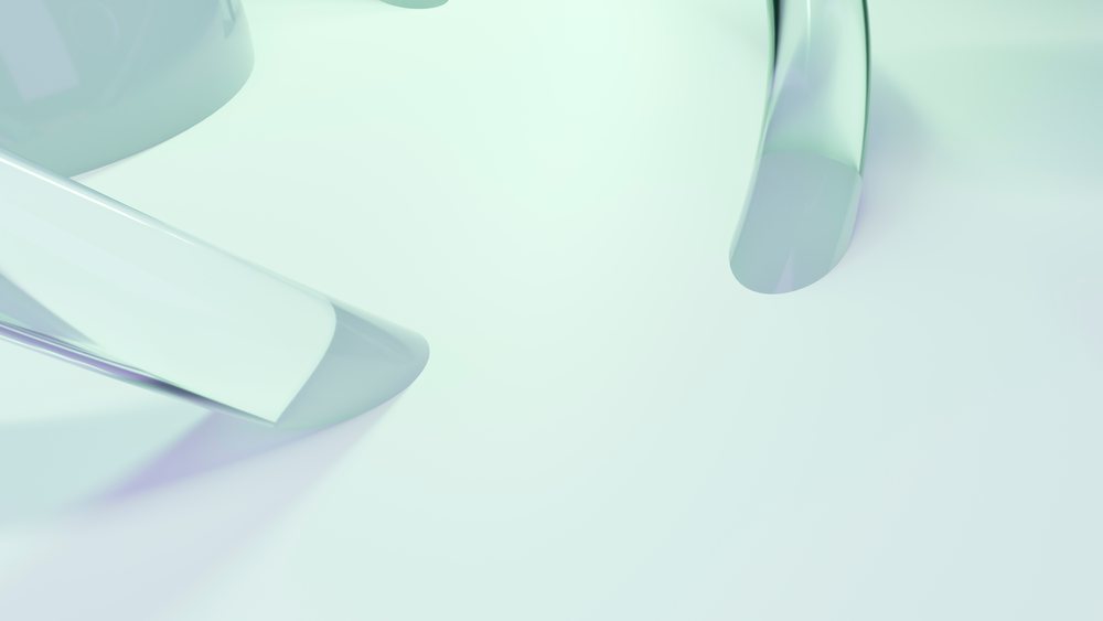 Abstract transparent glass shapes with smooth curved edges on a reflective surface in a minimalist studio setting under bright light.