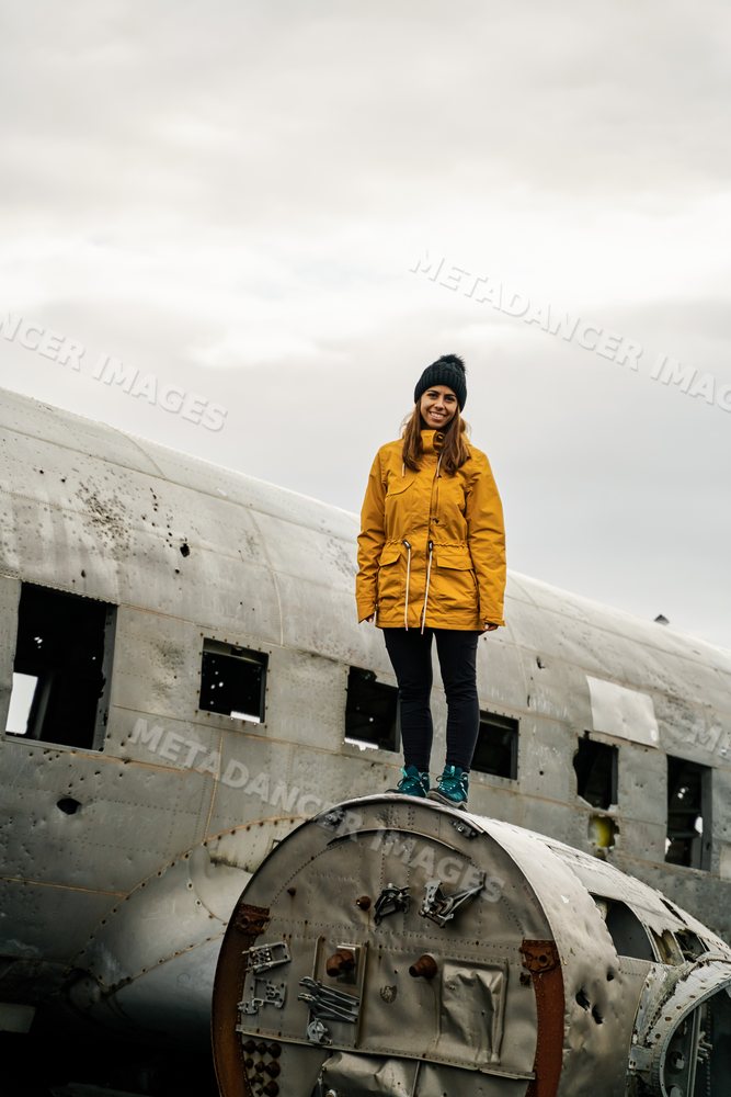 A white woman stands on a damaged airplane wreckage
