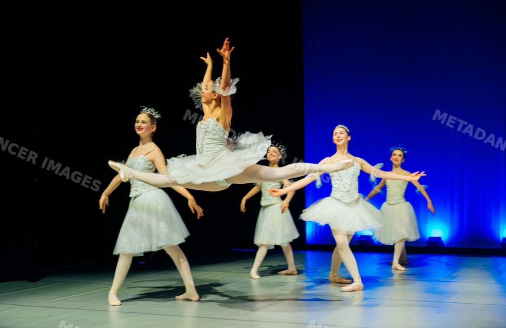 Ballet dancer performing a grand jeté leap on stage during recital