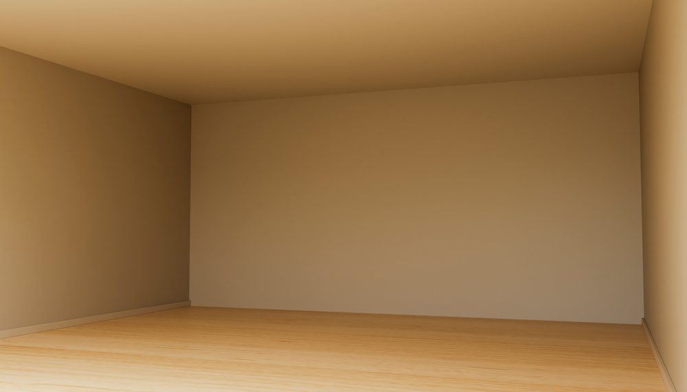 Empty room with wooden floor and beige painted walls seen from corner angle with natural lighting.