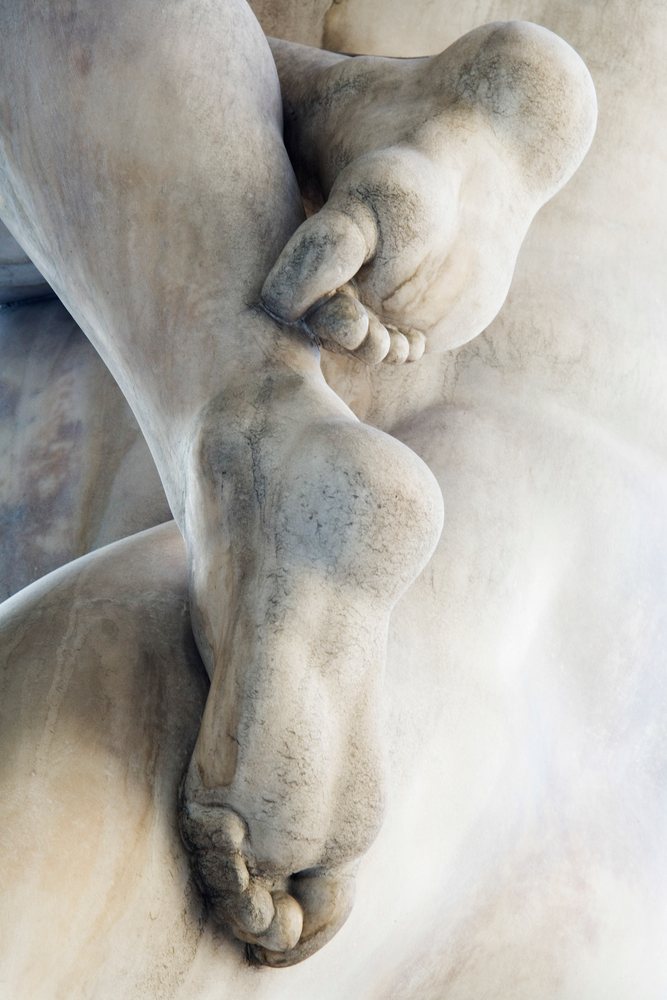 Close-up photograph of detailed feet on a weathered marble sculpture, Florence, Italy.