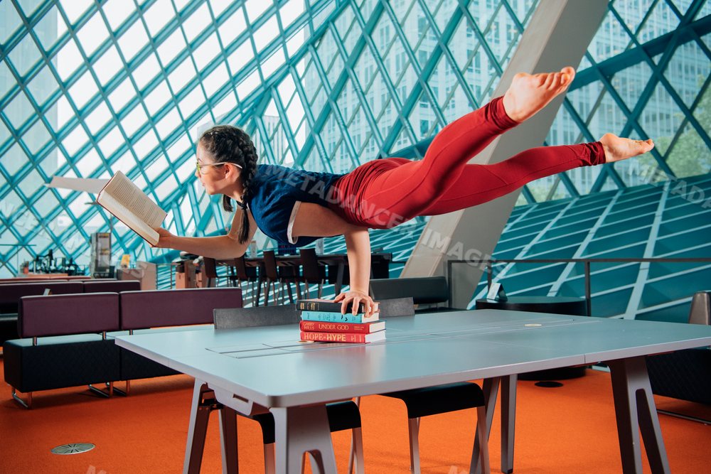 A woman balances in a handstand reading a book in a library