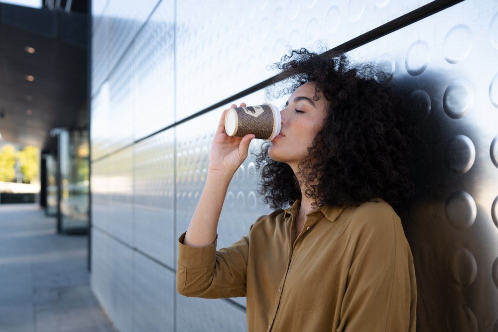 Woman with curly hair drinking coffee from a paper cup on an urban sidewalk, Madrid, Spain.