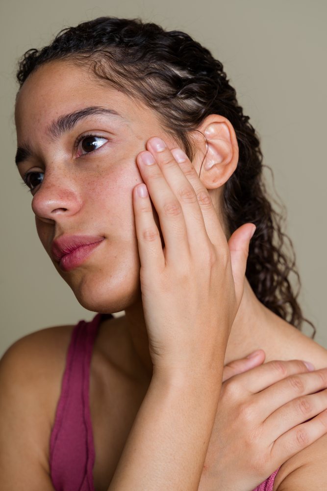Close-up portrait of a woman with curly hair and freckles touching her face indoors, beauty shoot, Spain.