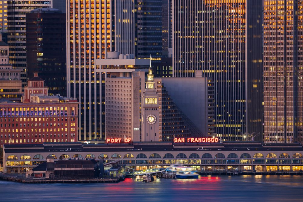 The Port of San Francisco ferry building with clock tower and city skyline illuminated at dusk along the waterfront pier, Cityscapes, City Life, California, USA.