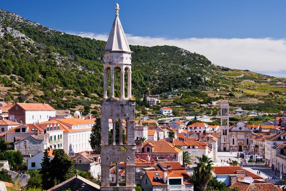 Town of Hvar with its stone bell tower and red tile roofs nestled below green Mediterranean hills, Croatia.