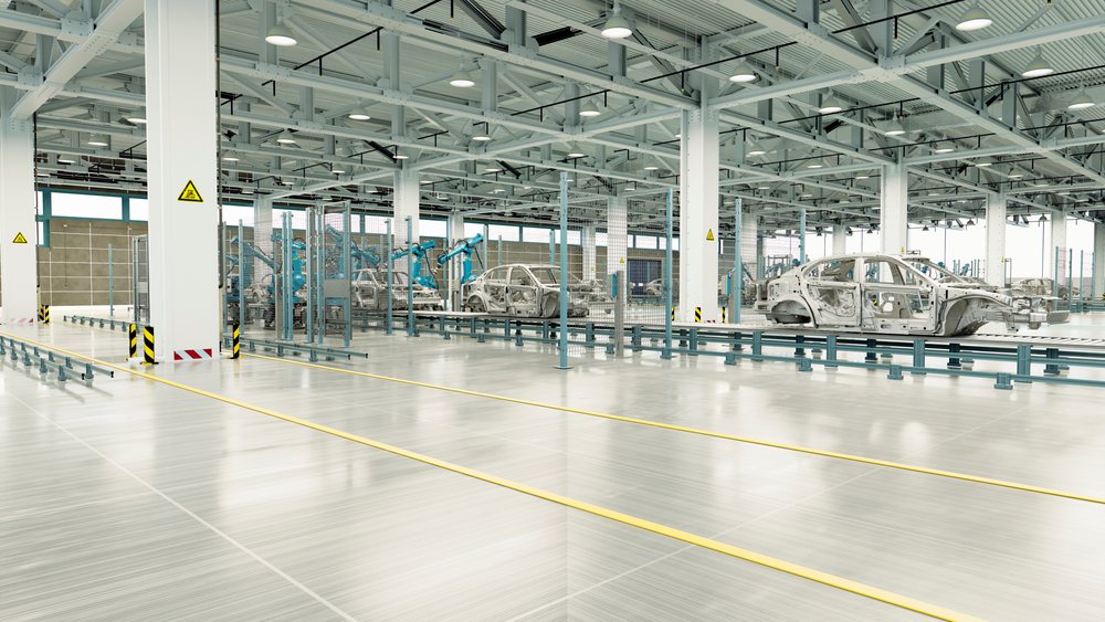 Interior of a modern car manufacturing factory with robotic arms assembling metal car frames on a conveyor system.