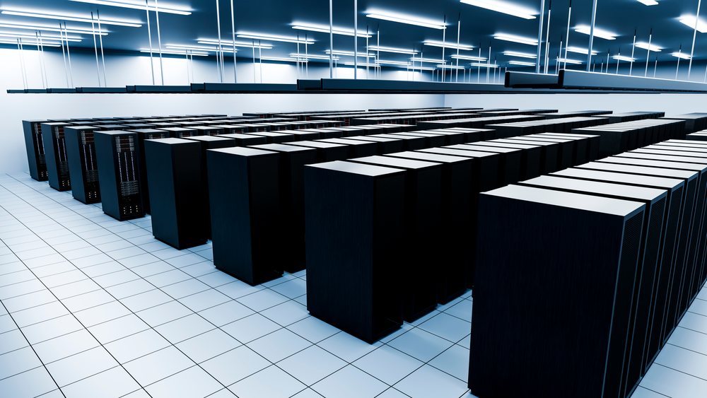 Data center room with rows of black server racks and ceiling cooling units in a modern facility.