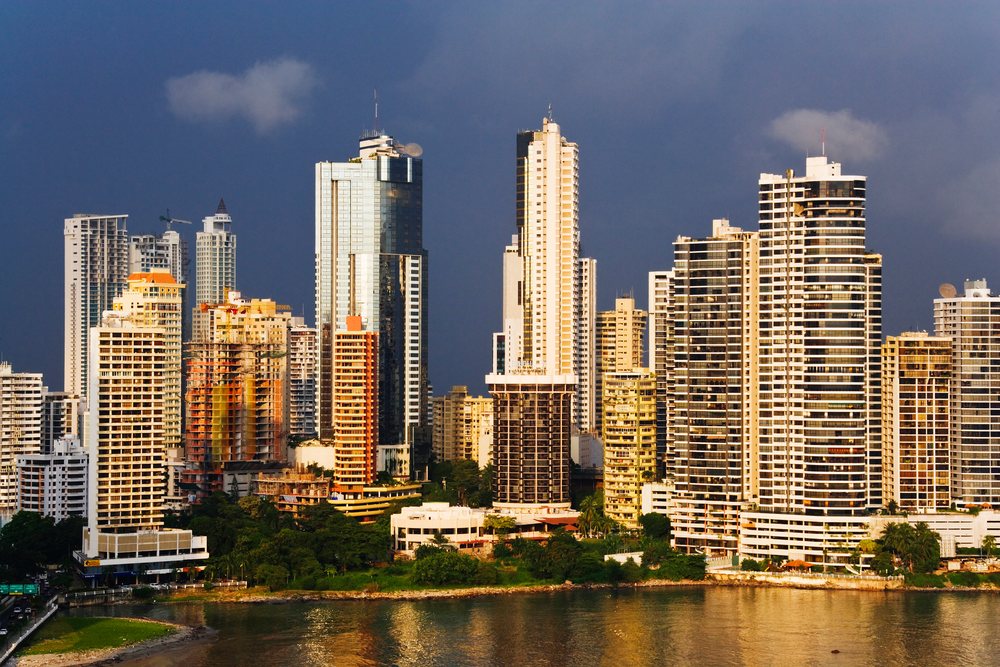 Panama City waterfront skyline features modern high-rise buildings reflecting under a dramatic sky.
