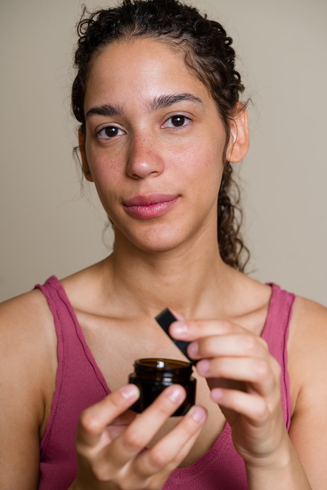 Woman holding an open jar of skin cream in a beauty shoot against a neutral background, Spain.