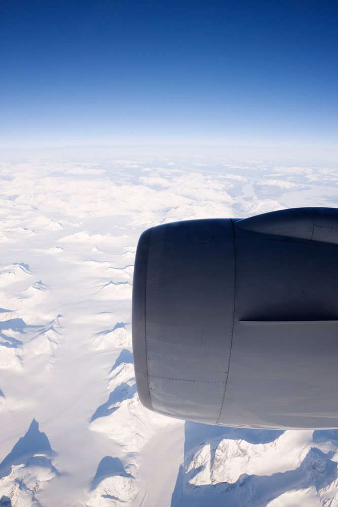 Boeing 777 airplane engine flying over a snowy mountain range under a clear blue sky at high altitude.