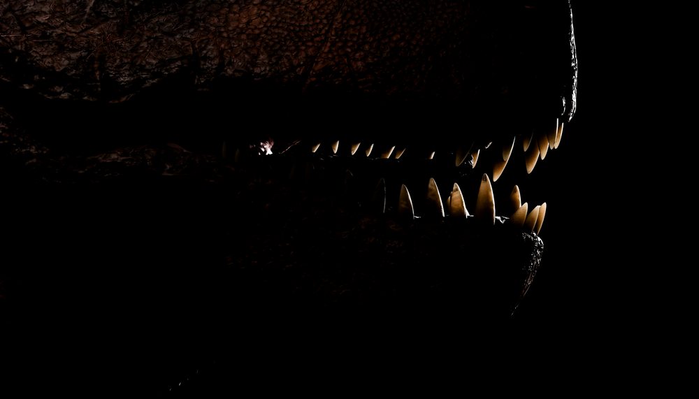 Close-up of a T-Rex mouth showing sharp teeth in dark lighting