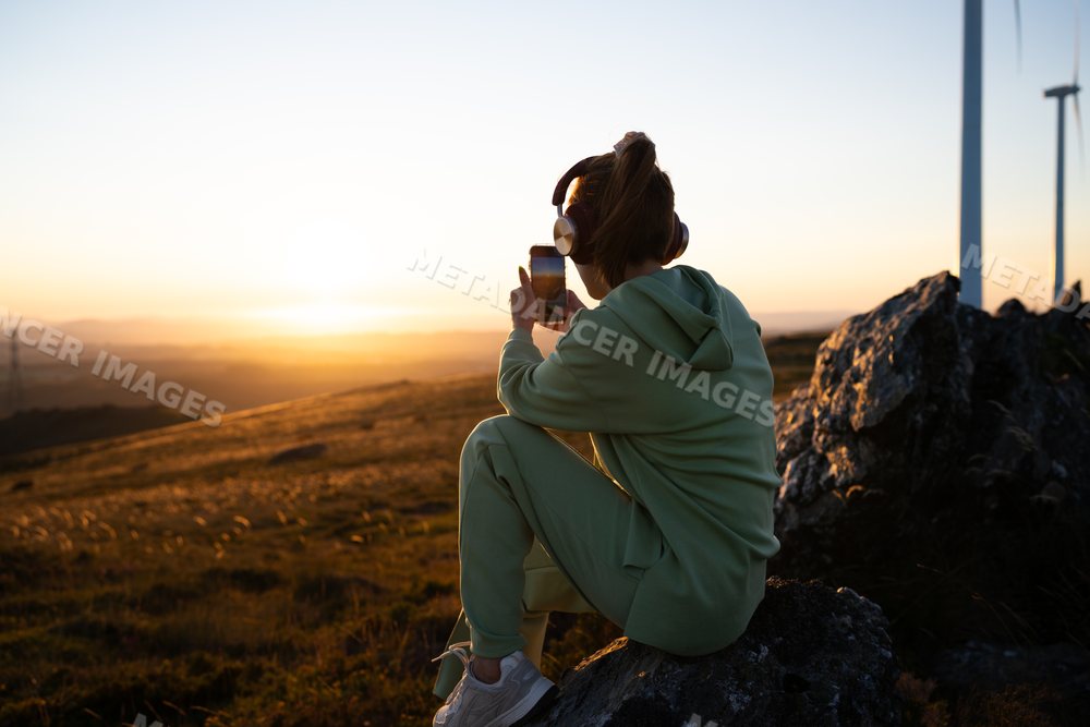 A white woman takes a photo at sunset near wind turbines in Galicia