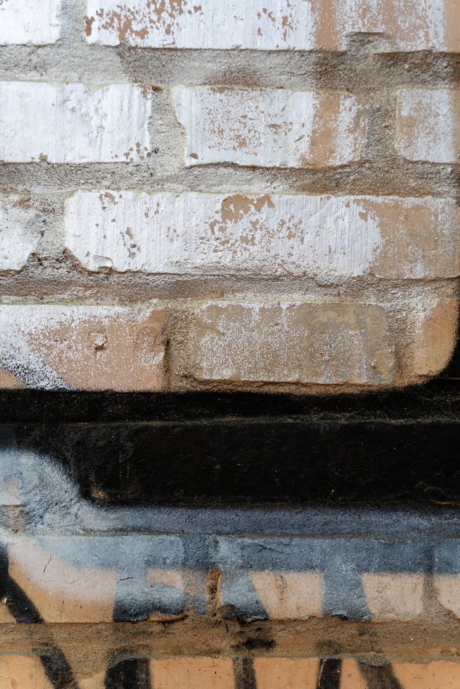 Close-up of a rough brick wall in Spain showing weathered white and black paint with peeling and textured surfaces, texture, abstract texture, background, wallpaper.