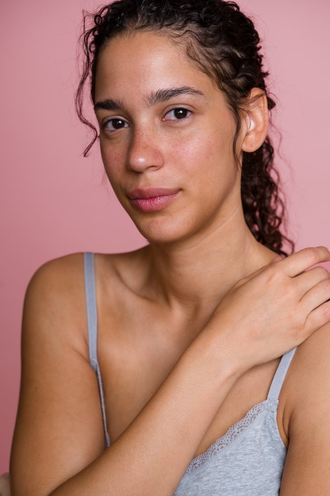 Woman with natural skin and curly hair poses against a pink background in a beauty studio setting, Spain.