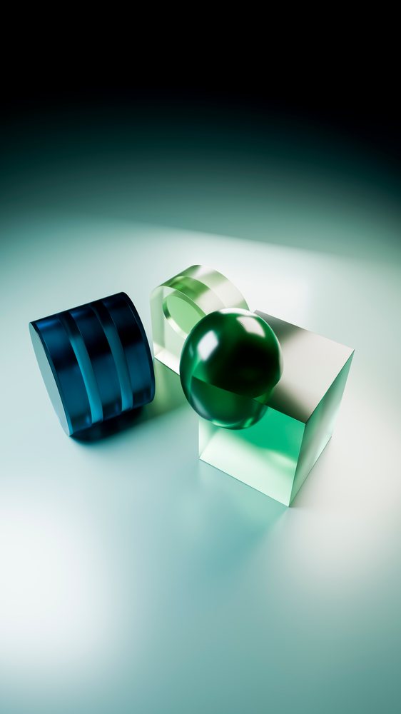 Green transparent sphere on a transparent cube beside a blue transparent cylinder arranged on a smooth reflective surface in an abstract digital illustration.