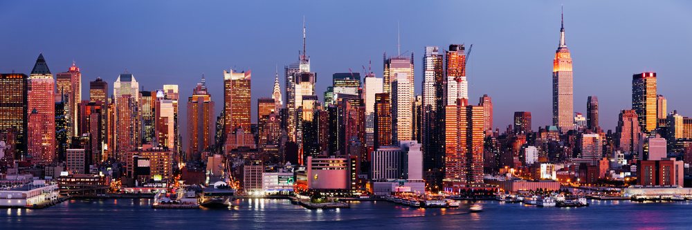 New York City Manhattan skyline viewed at sunset with illuminated skyscrapers reflecting on the waterfront, USA.