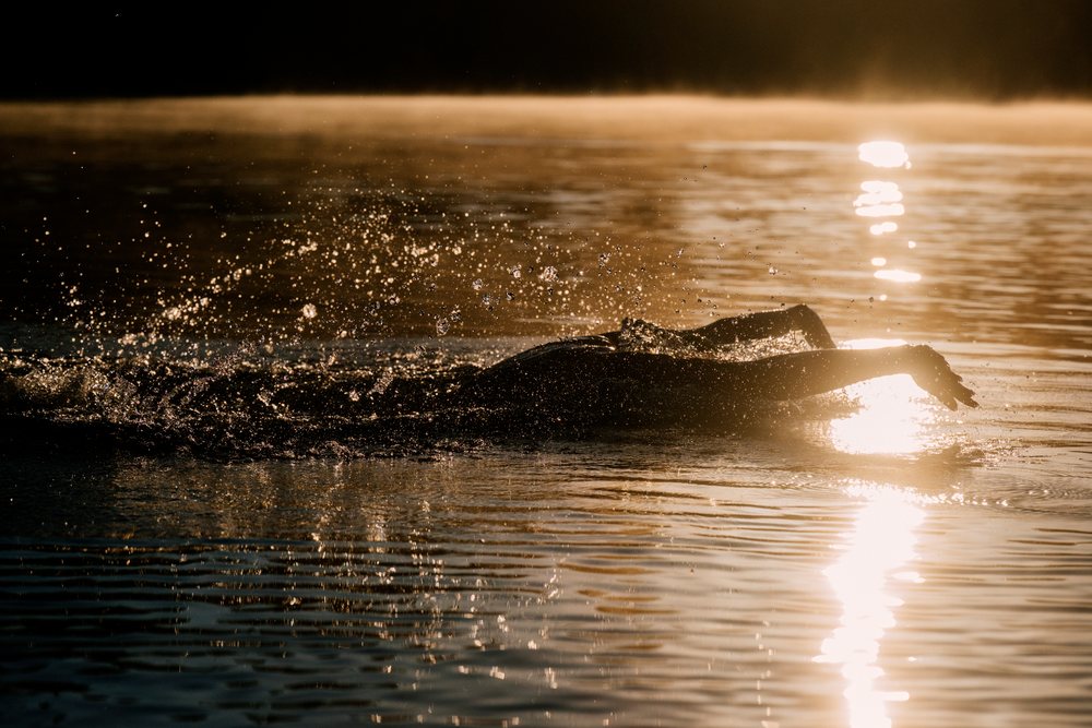 Swimmer performing a stroke in water at sunrise with splashing droplets visible in an outdoor lake, USA.