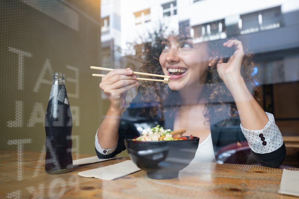 Woman eating Asian food with chopsticks and smiling inside a restaurant, businesswoman, traveling executive, Spain.