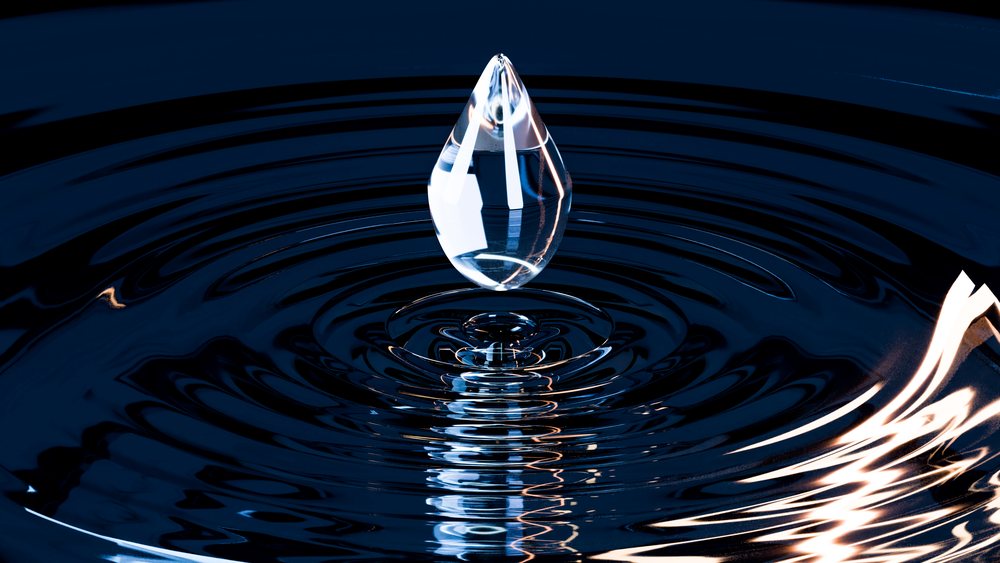 Transparent water droplet suspended above a dark blue water surface with circular ripples and reflections.
