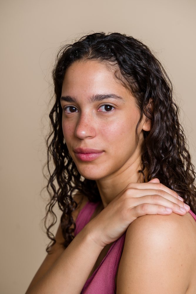 Portrait of a woman with curly hair and freckles wearing a pink sleeveless top in a beauty shoot, Spain.
