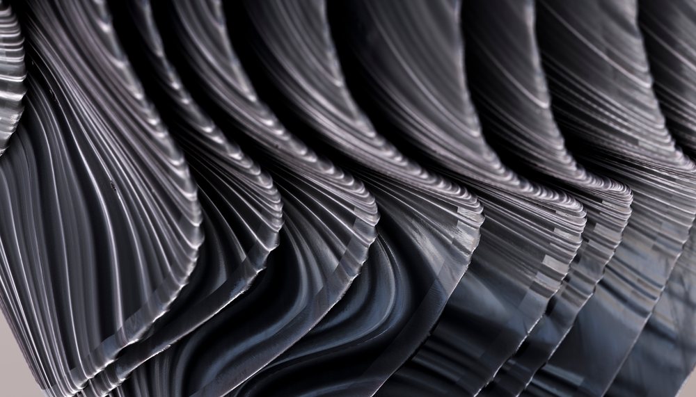 Closeup of a wavy black metal sculpture with reflective curved surfaces in a studio setting.