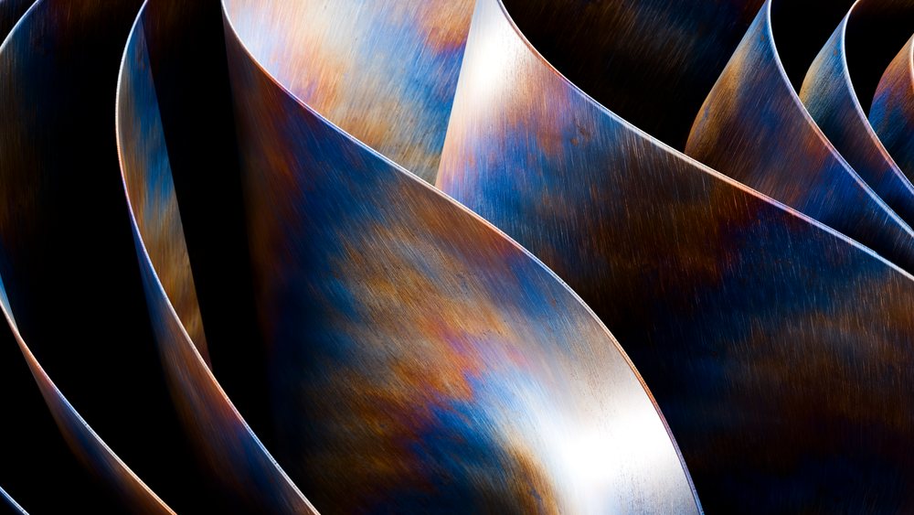 Curved metal sculpture with blue and orange patina creating an abstract artistic effect.