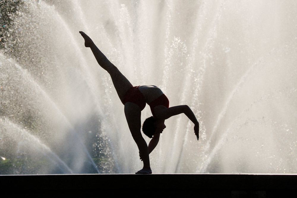 Silhouette of a woman performing a balanced one-legged yoga pose before a fountain spraying water, USA.
