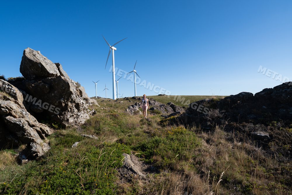 A white woman hiking near wind turbines in a rocky landscape