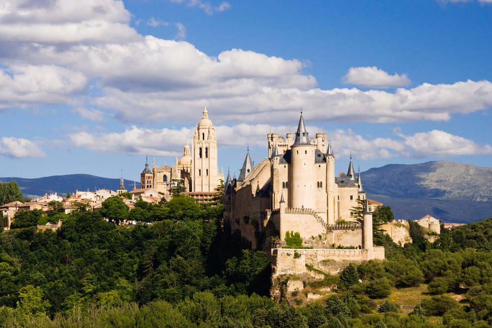 Alcazar castle with multiple towers stands atop a hill.
