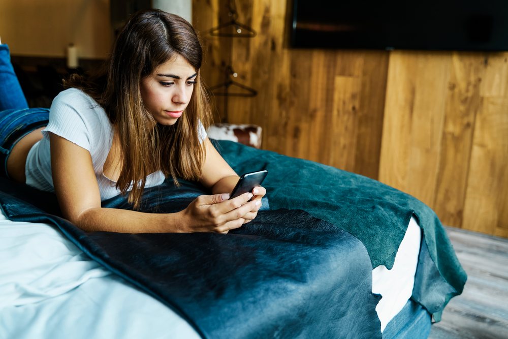 A woman relaxes using her smartphone in a hotel room in a hotel