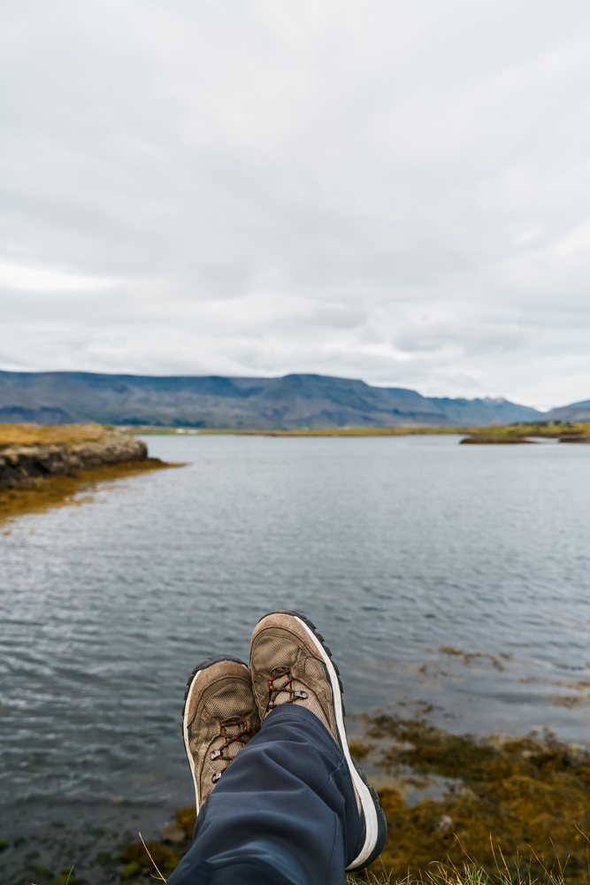 Person relaxing by a lake with hiking boots