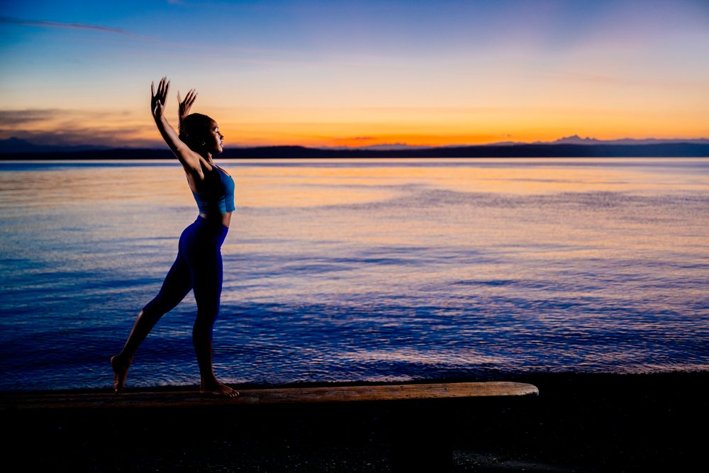 Woman practicing a yoga balance pose at sunset on a bench near a lake, USA.