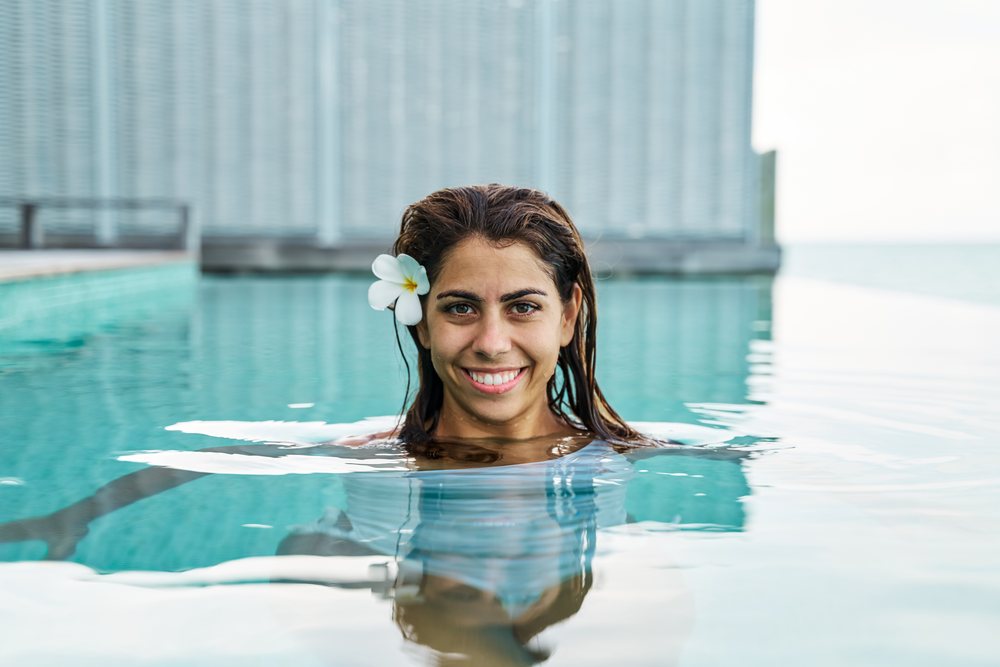 A smiling white woman enjoys relaxing in an outdoor pool at a resort