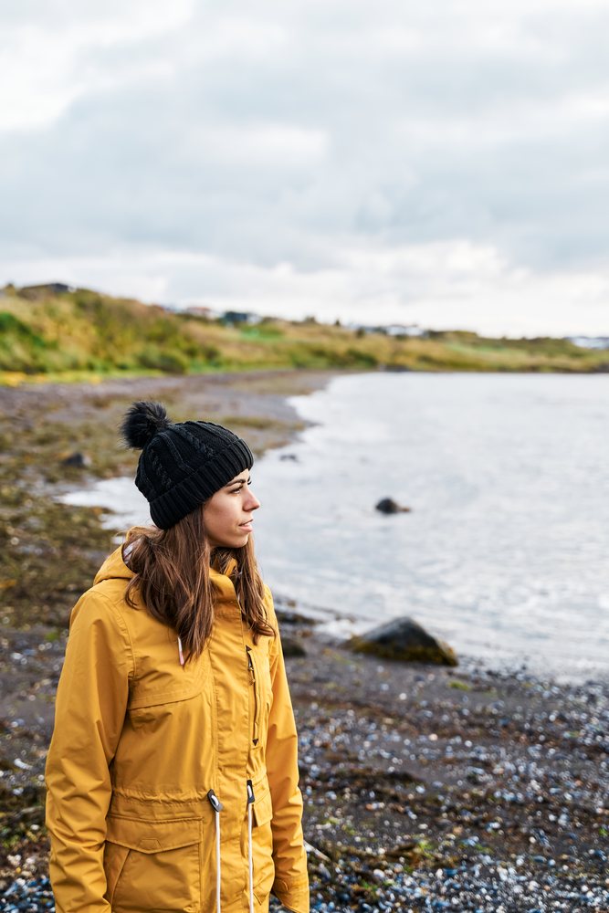 A white woman stands on a rocky coastal shore