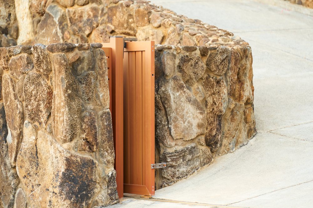 Stone wall with wooden gate along curved cement pathway outdoors, Oahu, Hawaii, USA.