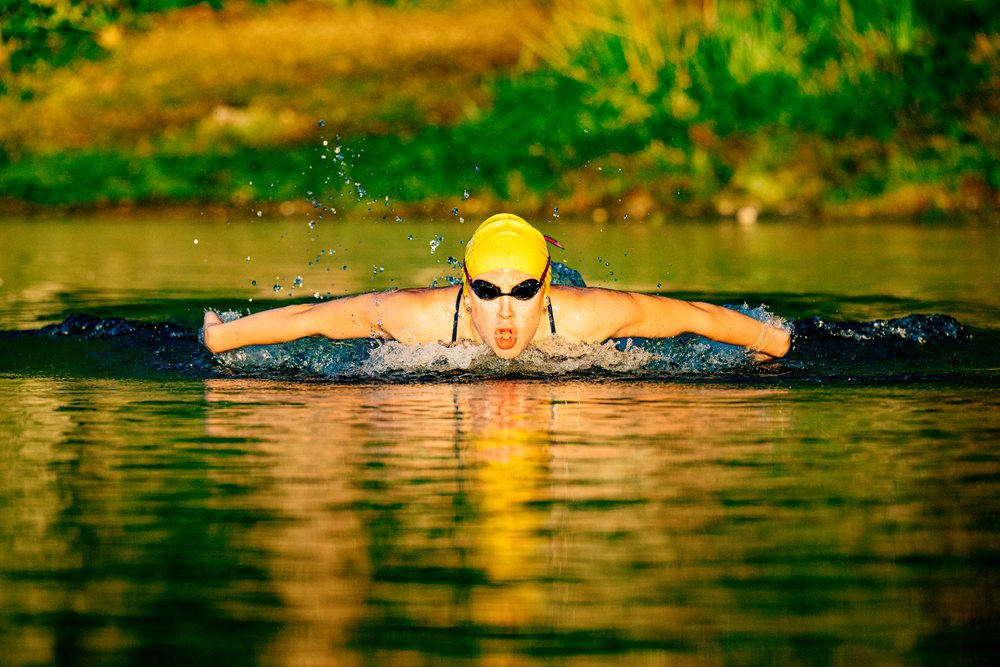 Swimmer performing butterfly stroke in open water with splash and sunset lighting, USA.