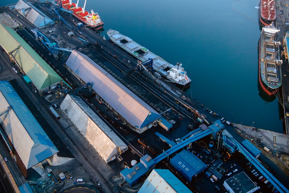 Aerial view of a major commercial port showing cargo ships docked by industrial buildings and storage warehouses, a major commercial port, CA, USA.