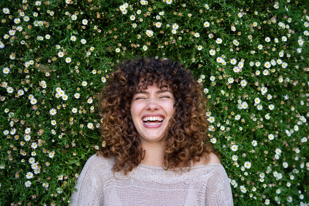 Woman with curly hair lies laughing in a field of white daisy flowers, home story, influencer, Spain.